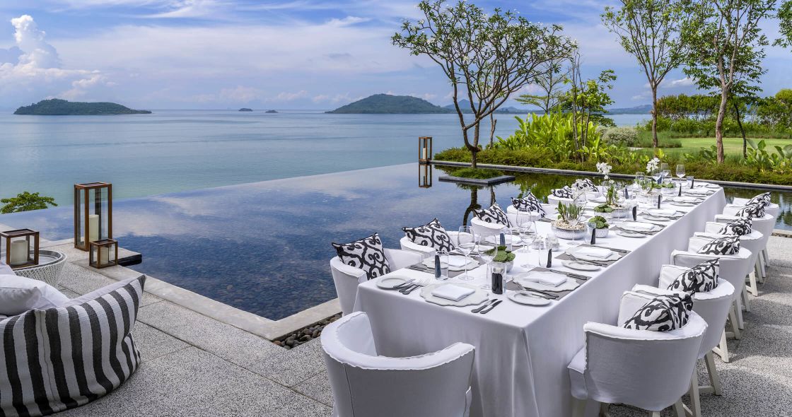 A Table Set With White Cloths And White Tables Overlooking A Body Of Water