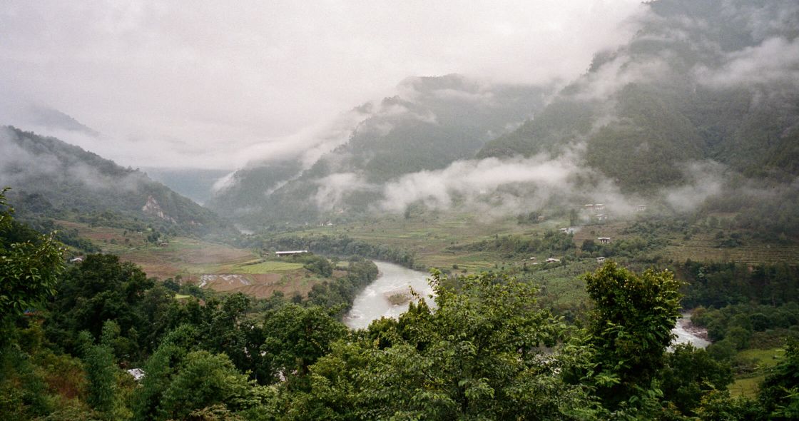 A River Running Through A Valley With Trees And Mountains In The Background