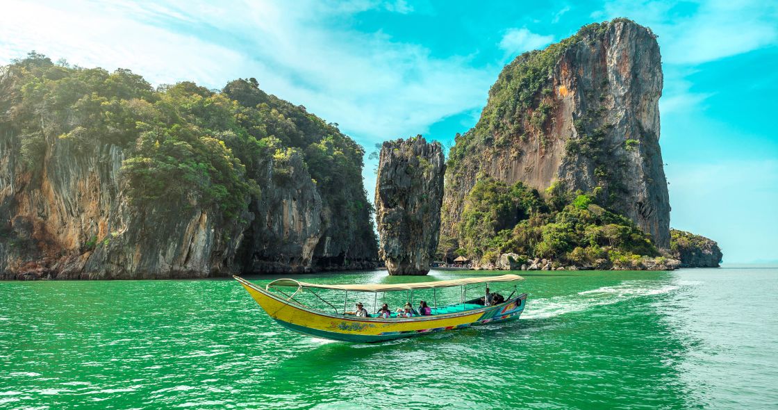 A Boat In The Water With Large Rocks In The Background With Phi Phi Islands In The Background
