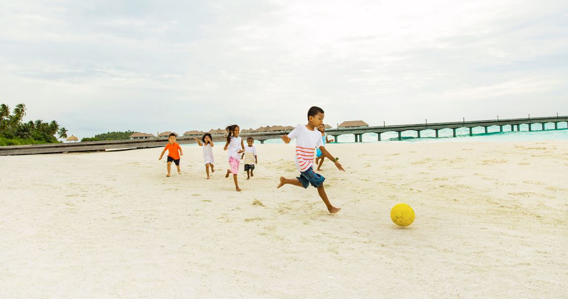 A Group Of Kids Playing Football On A Beach