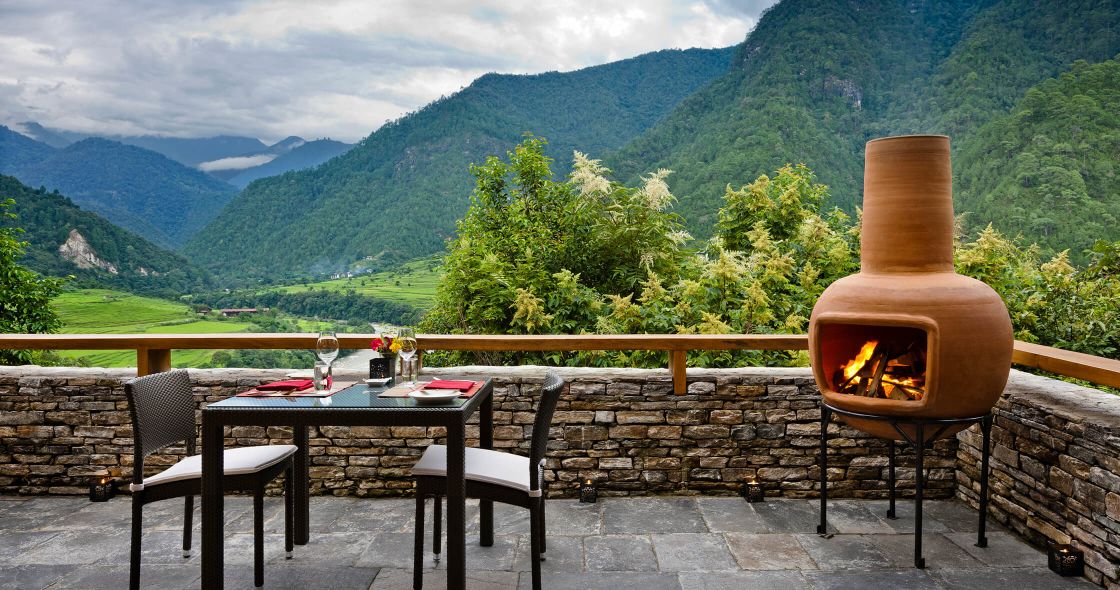 A Table With A Fire In Front Of A Fire Pit With Trees And Mountains In The Background