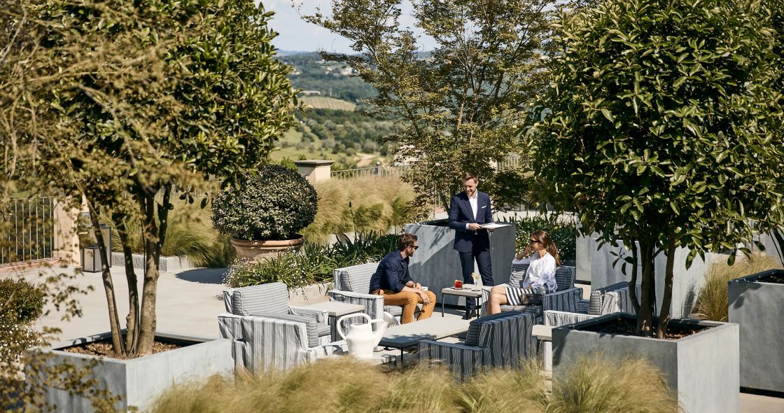 A Group Of People Sitting On A Patio With Trees And Plants
