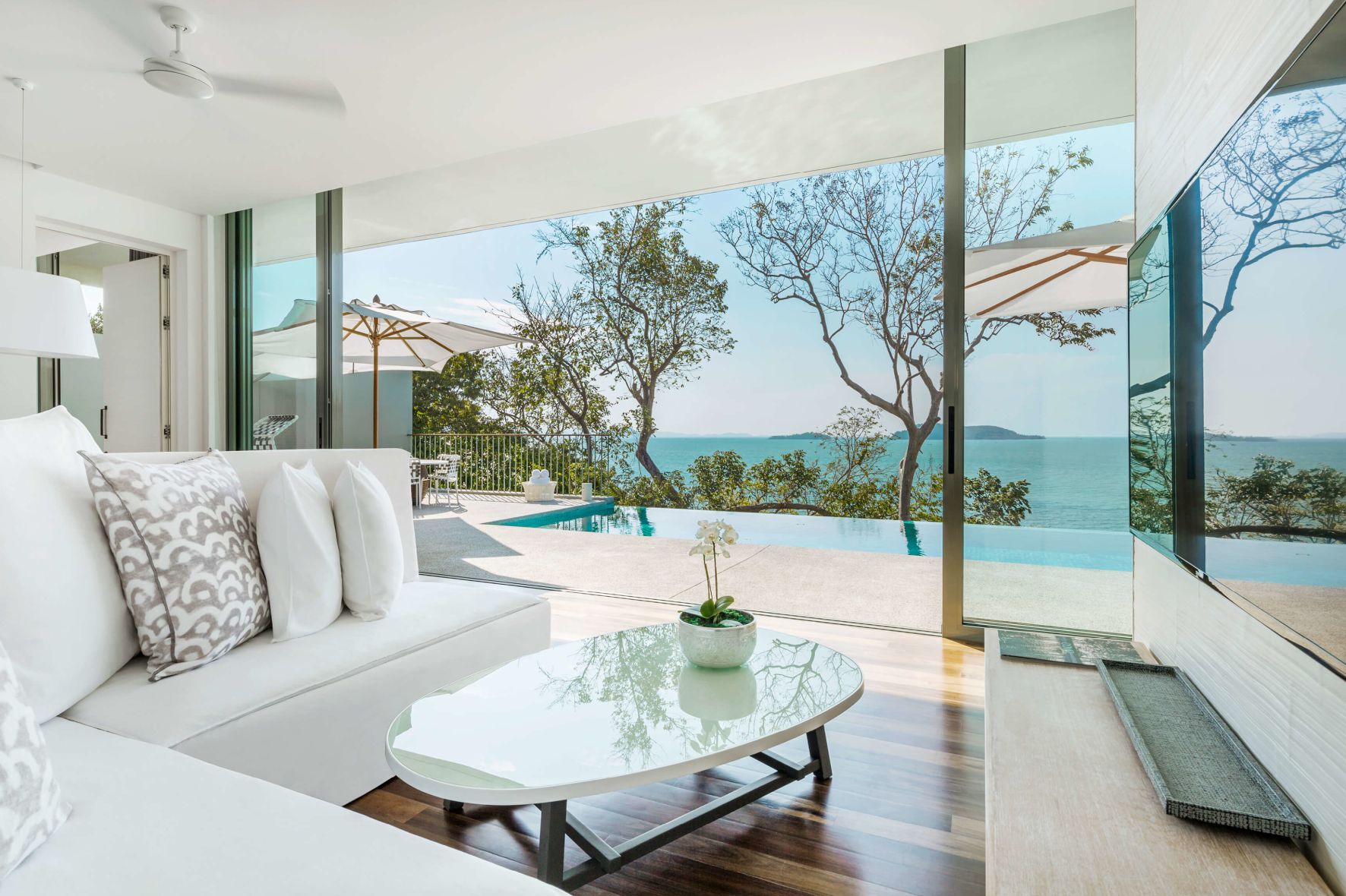 A Room With A Pool And A Large Window With Trees And A Body Of Water In The Background