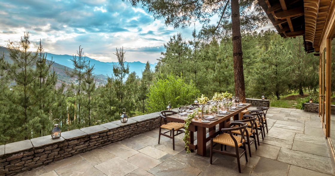 A Patio With A Table And Chairs And A Wood Deck With Trees And Mountains In The Background