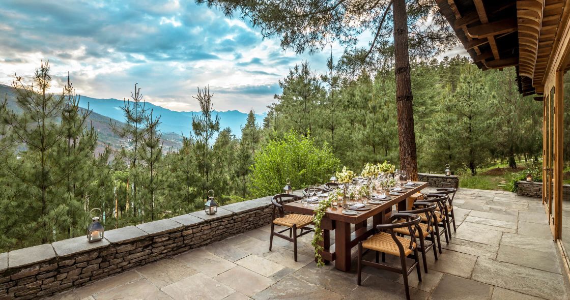 A Patio With Tables And Chairs And A Wood Deck With Trees And Mountains In The Background