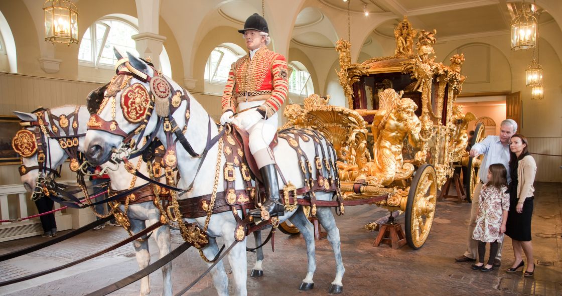 A Person Riding A Horse With A Carriage Attached To It With Royal Mews In The Background