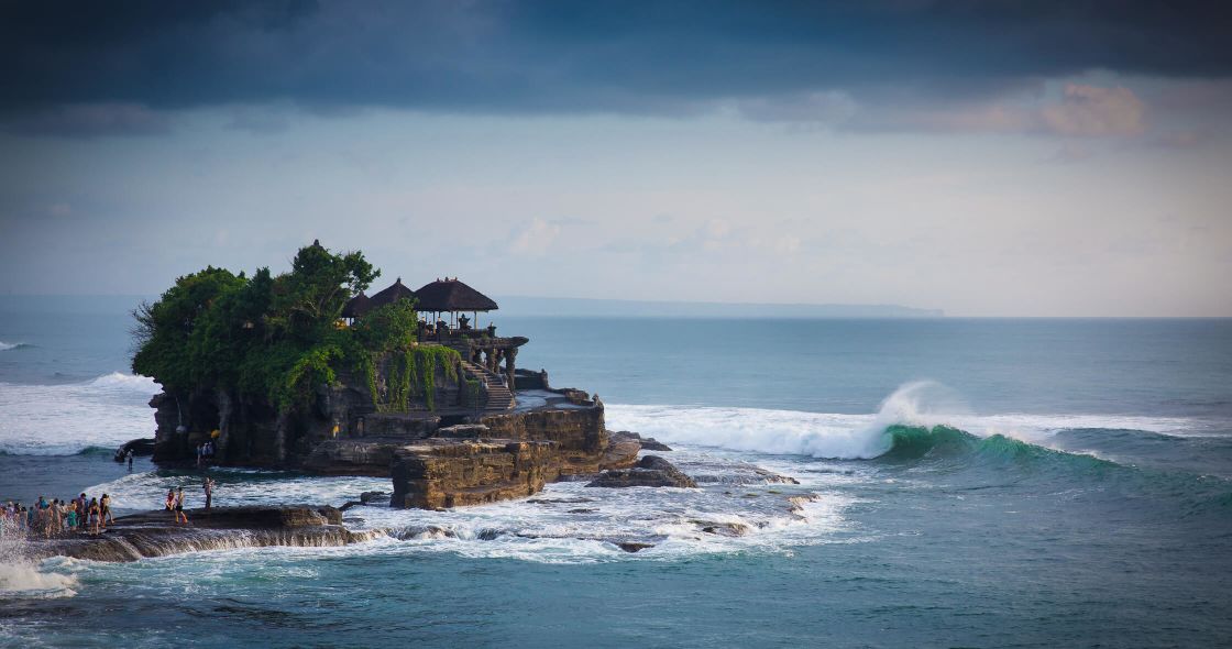 A Group Of People On A Rocky Beach With Tanah Lot In The Background