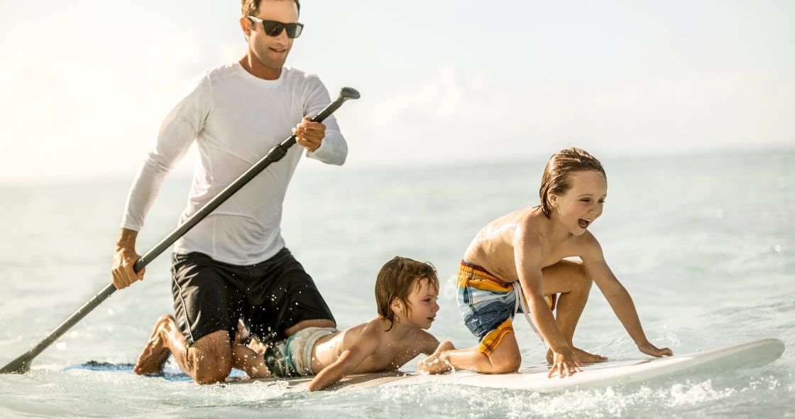 A Man And Two Kids On A Surfboard