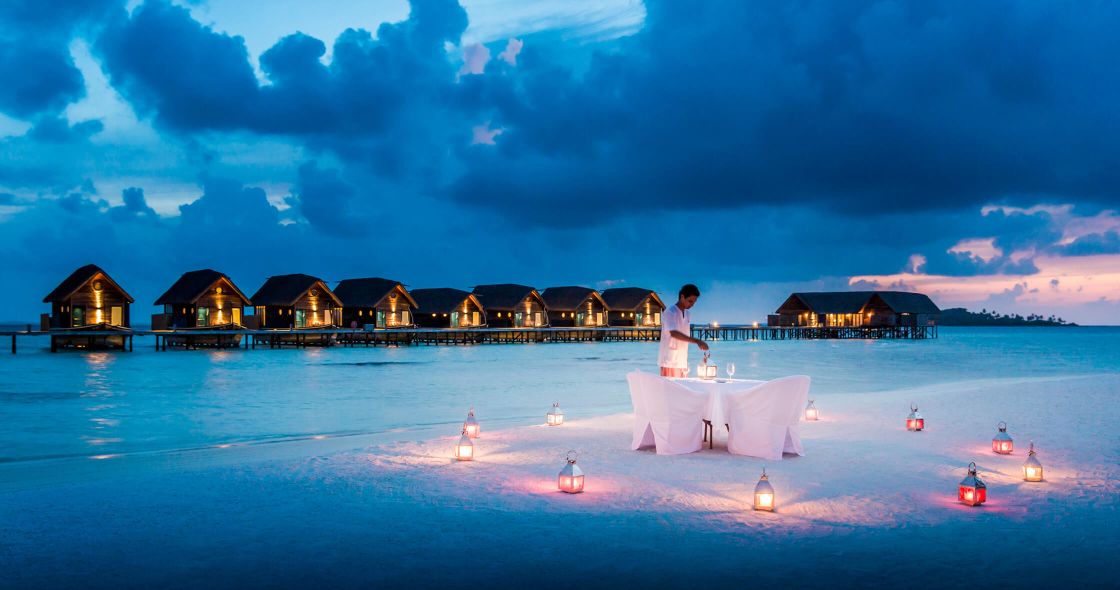 A Person Standing On A White Platform Surrounded By Water With A Row Of Lit Up Buildings In The