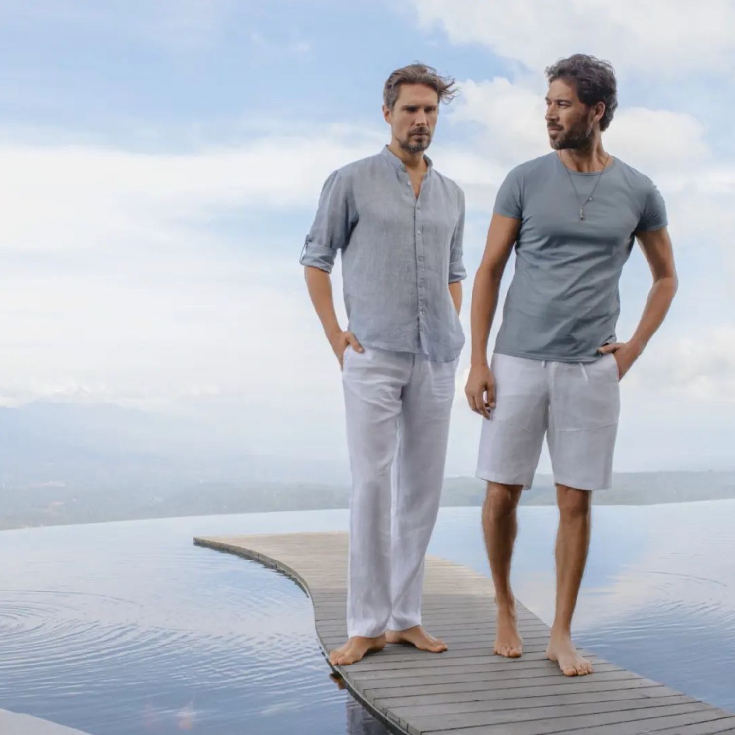 A Couple Of Men Standing On A Dock With Water And A Cloudy Sky