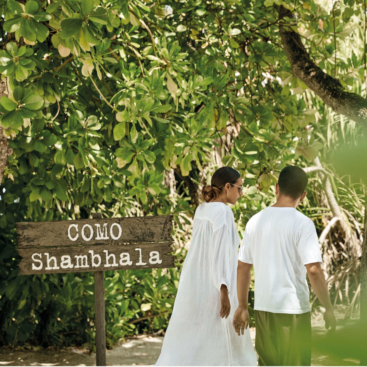 A Man And Woman Walking Down A Path With A Sign And Trees