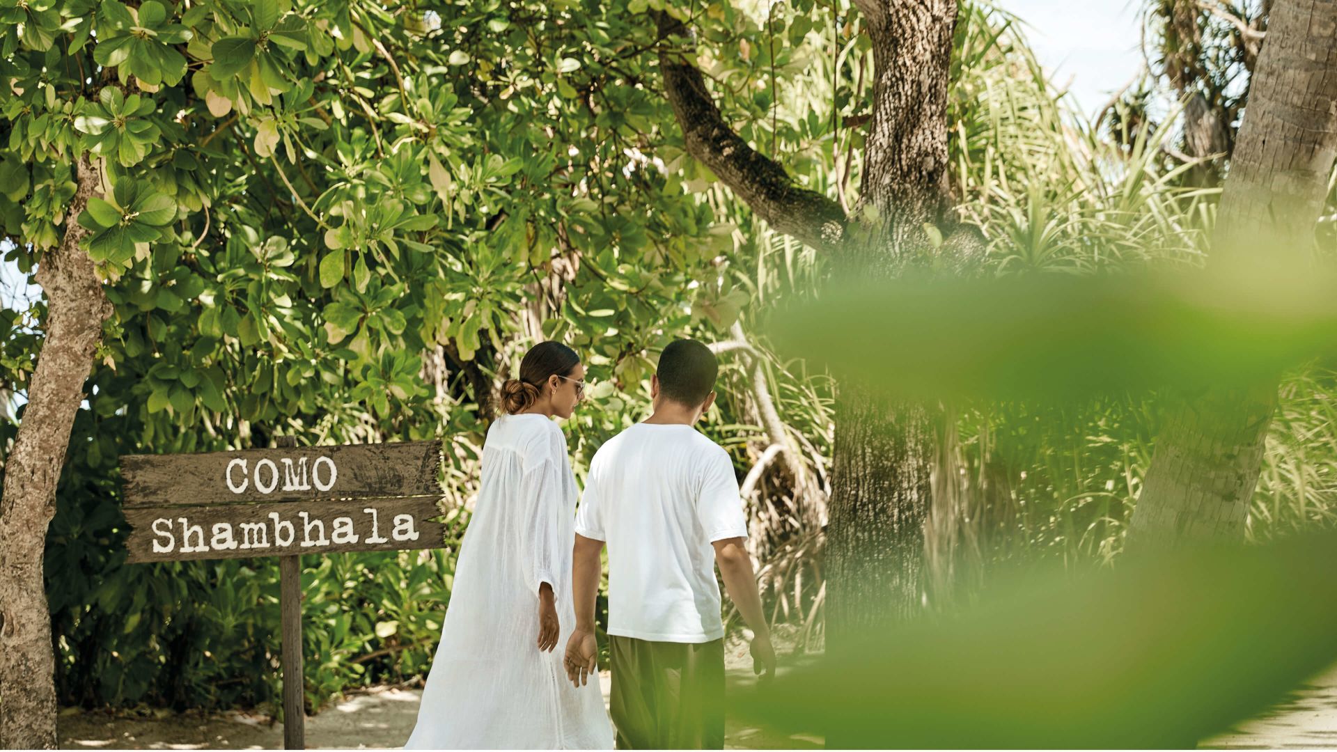 A Man And Woman Walking Down A Path With A Sign And Trees