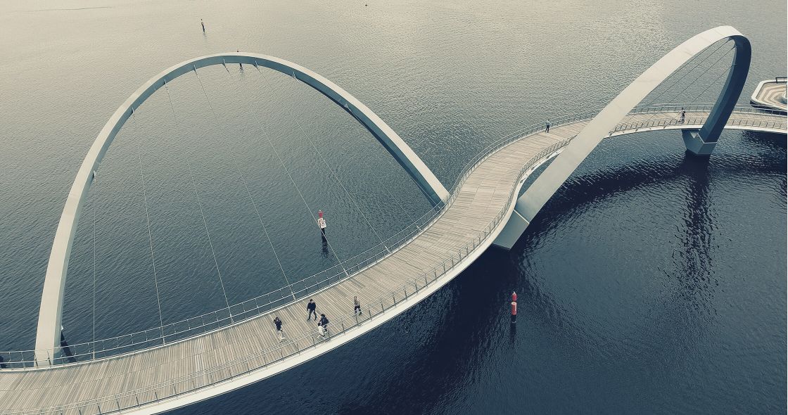 A Group Of People Walking On A Bridge Over Water