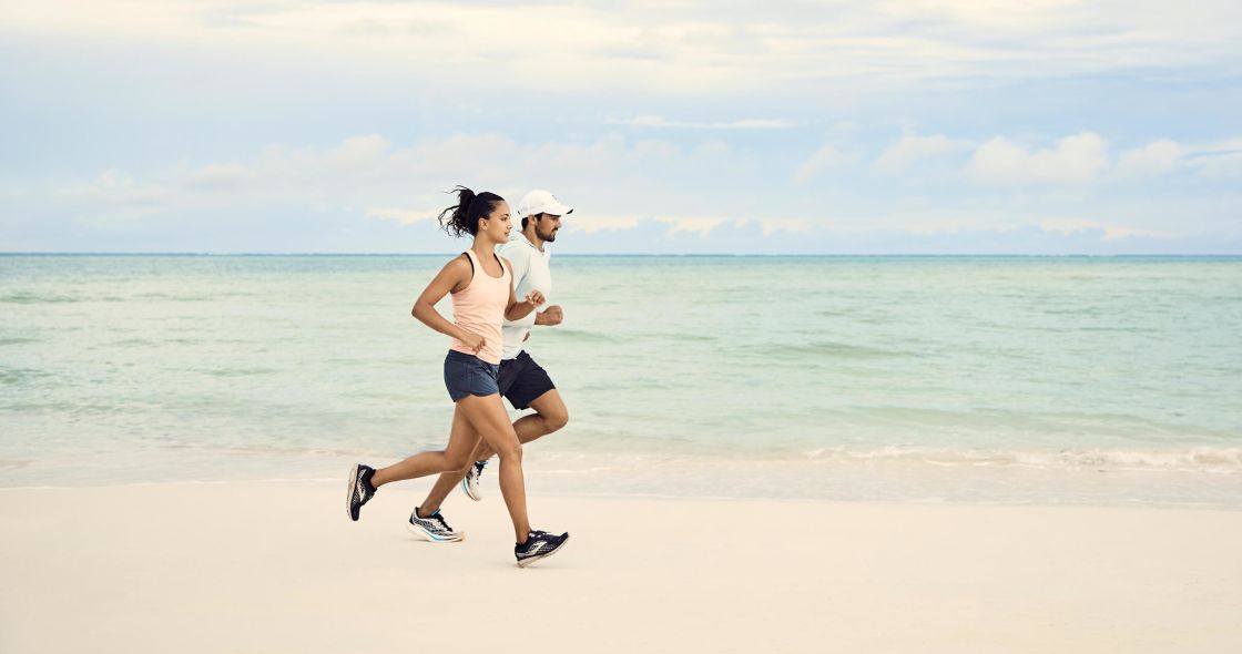 A Man And Woman Running On A Beach